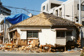 屋根の瓦が半分以上崩れ落ち、葺き土の下にある野地板が剥き出しになった一軒家